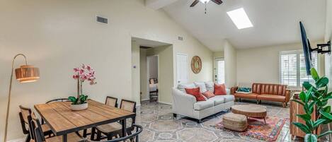 A spacious living area with a dining table, chairs, a white sofa, and a brown leather couch.