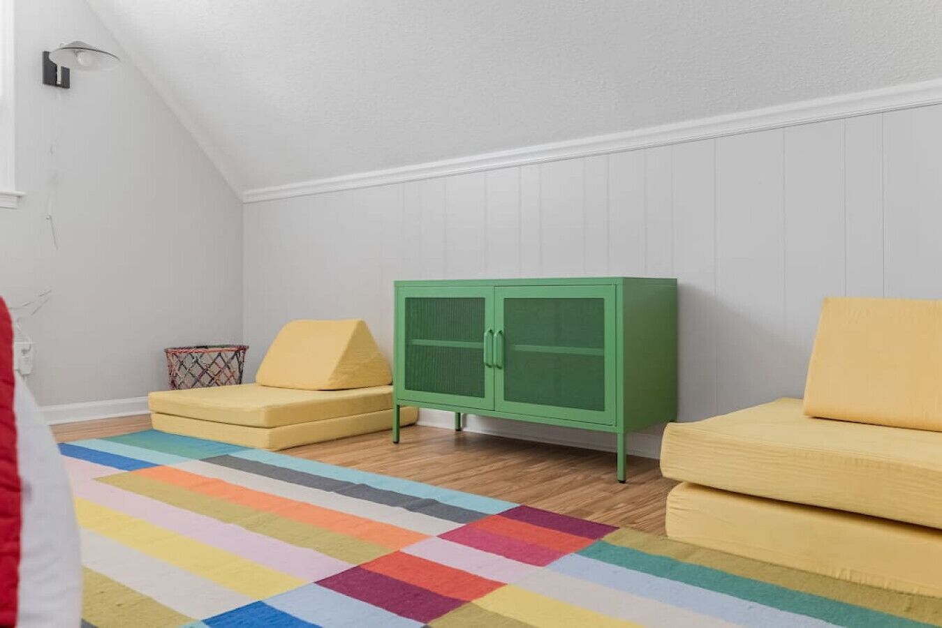 A room with a green cabinet, two yellow sofas, and a colorful striped rug.