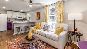 A modern living room with a white sofa, yellow cushions, a patterned rug, and a ceiling fan. - Charming creekside retreat in historic Burlington (Burlington)