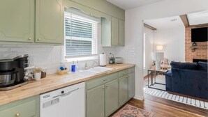 A kitchen with green cabinets, a dishwasher, and a window with blinds.
