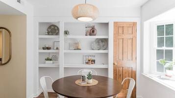 A dining area with a round table, white chairs, a wooden door, and a window with a view.