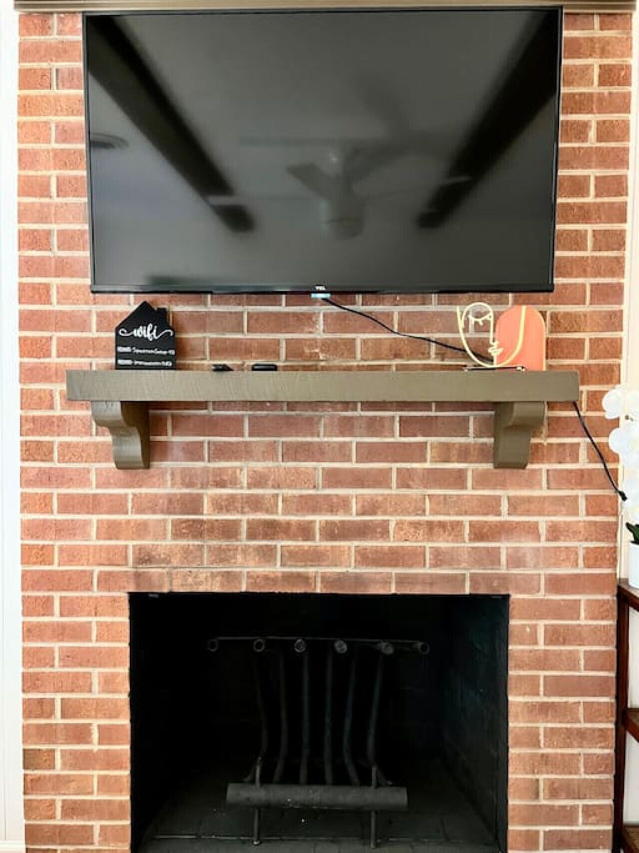 A brick fireplace with a flat-screen TV mounted above it, a shelf below, and a small sign indicating wifi availability.