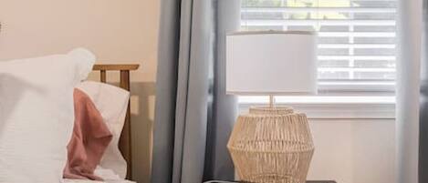 Una camera da letto con un letto, un comodino con una lampada e una finestra con tende.