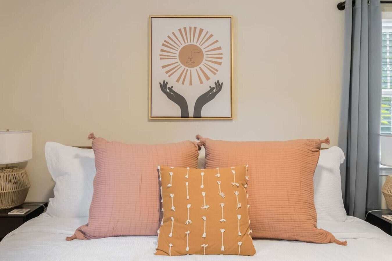 A neatly made bed with two large pillows and a smaller decorative pillow, a framed artwork above the bed, and a lamp on a bedside table.