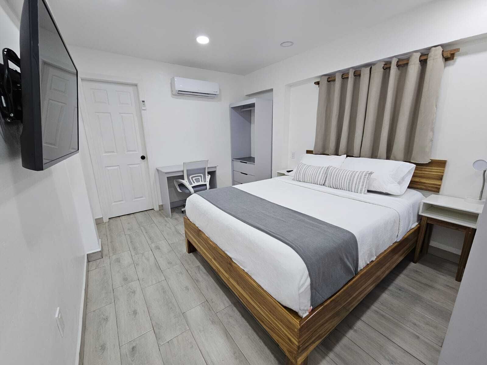 A bedroom with a bed, bedside table, chair, desk, and a TV mounted on the wall.