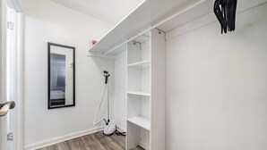 Ein Flur mit einer weißen Tür, einem gerahmten Bild an der Wand und einem weißen Regalschrank mit Staubsauger.