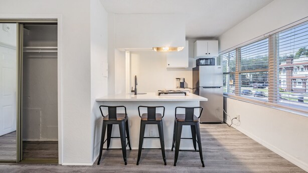 Eine moderne Küche mit weißer Arbeitsplatte, drei schwarzen Barhocker und einem großen Fenster mit Ausblick.