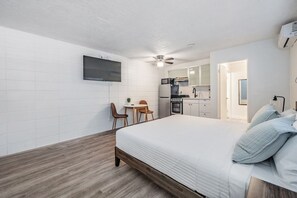 Une chambre d’hôtel compacte comprenant un lit, une petite kitchenette, un téléviseur fixé au mur et un ventilateur de plafond.