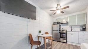 Eine kompakte Küche mit weißen Schränken, einem eingebauten Backofen, einer Mikrowelle und einem Deckenventilator.
