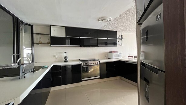 Uma cozinha moderna com armários preto e branco, eletrodomésticos de aço inoxidável e bancada branca.