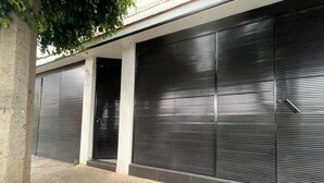 Fachada de edifício com portas fechadas e protegidas por portões, um pilar de concreto e uma árvore acima.