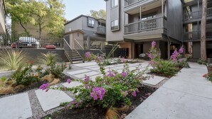 A modern multi-story building with balconies and a landscaped courtyard featuring purple flowers. - UT North Campus Apt Unit 12 /1 Mile to Moody Center
 (Austin)