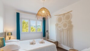 Une chambre avec un grand lit, une fenêtre avec des rideaux, une décoration murale en macramé et un luminaire suspendu.
