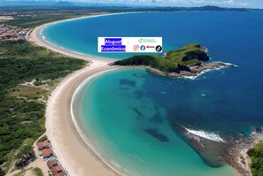 An aerial view of a coastal area with a beach, a small island, and a town in the background.