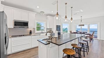 A spacious kitchen with white cabinetry, a large island with bar stools, and a view of the ocean.