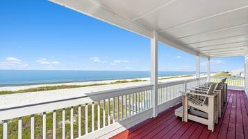 A covered porch with a red floor and white railings, overlooking a beach and ocean.