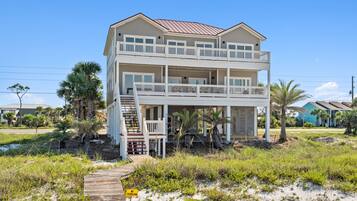 A two-story beachfront house with a balcony, a wooden deck, and a 'No Swimming' sign.