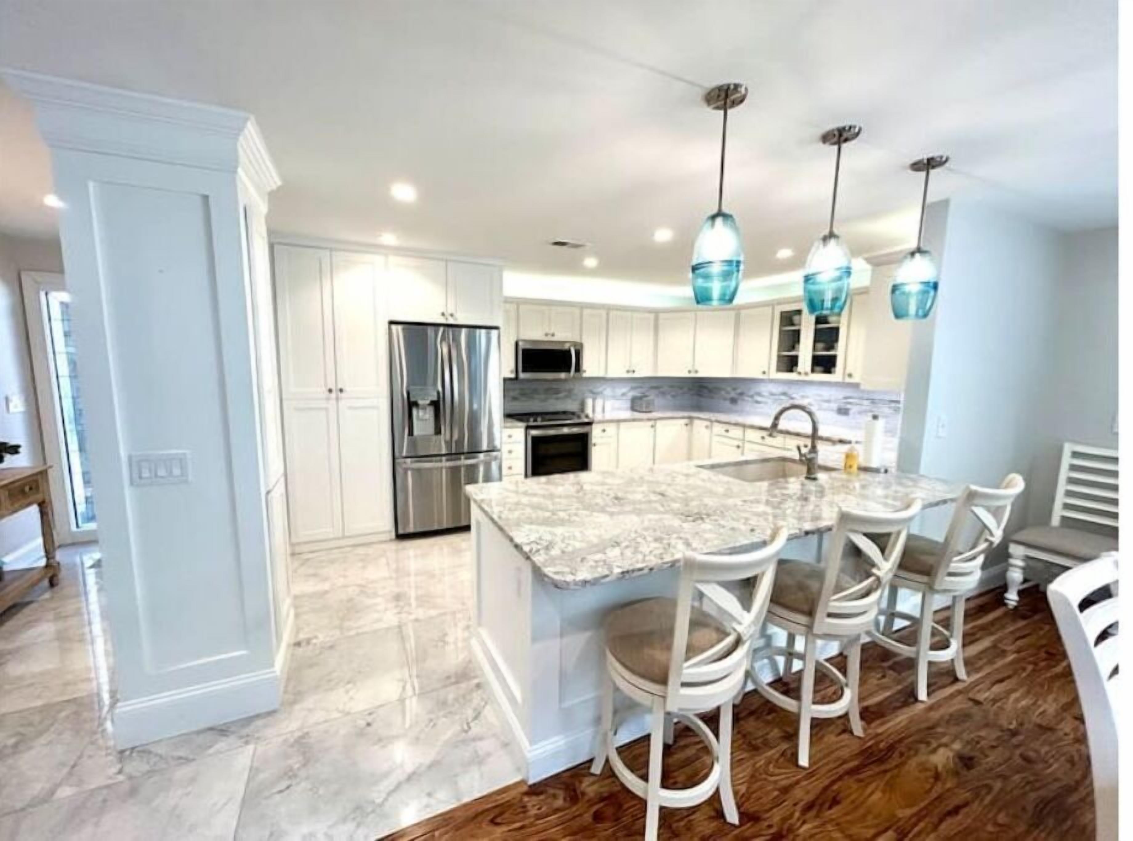 A modern kitchen with white cabinetry, stainless steel appliances, and a marble countertop.