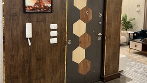 Une pièce avec un mur en bois, une porte ornée d’un motif géométrique, un tableau encadré représentant la Tour Eiffel et un téléphone blanc fixé au mur.