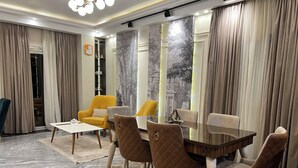Un coin repas avec une table et des chaises, un fauteuil jaune et une grande fenêtre avec des rideaux.