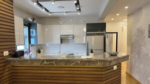 Une cuisine moderne dotée d’un plan de travail en marbre, d’appareils électroménagers intégrés et d’un mur d’accent en bois.