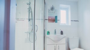 Ein Badezimmer mit Duschkabine aus Glas, Waschbecken in Weiß und Toilette.