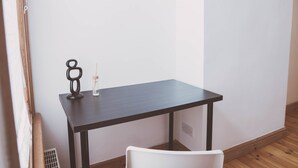 Ein kleiner, dunkler Holztisch mit einem weißen Stuhl in einer Ecke eines Raumes mit Holzboden und weißen Wänden.