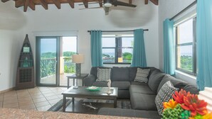 Een woonkamer met een bank, een salontafel en een lamp. Er is een balkon met uitzicht op zee.