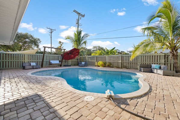 Patio trasero con piscina, valla de madera y zona de estar techada.