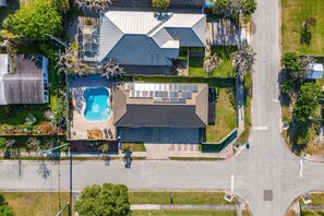 Vista aérea de una propiedad residencial con piscina, una casa grande de techo inclinado y un césped bien cuidado.