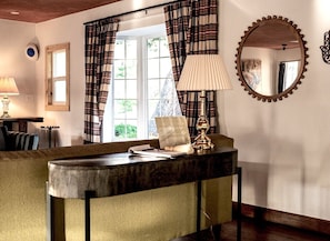 Una habitación con escritorio de madera, lámpara, espejo y cortinas a cuadros.
