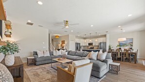 A spacious living room with a gray sectional sofa, a wooden coffee table, and a modern ceiling fan.