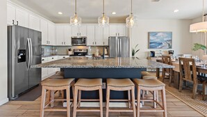 A modern kitchen with a large island, stainless steel appliances, and pendant lighting.