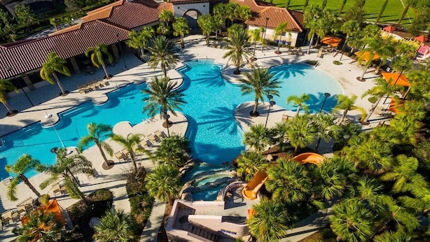 An aerial view of a resort with multiple swimming pools, palm trees, and a central water feature.