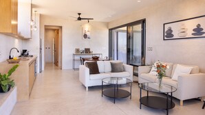 Una sala de estar moderna con un sofá blanco, dos mesas de centro de vidrio y una zona de comedor al fondo.