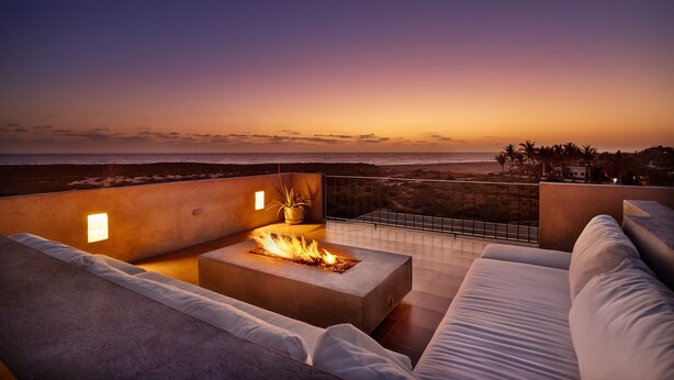 Terraza en la azotea con una chimenea, asientos y vista a la playa al atardecer.