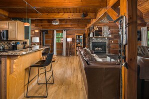 A log cabin interior with a kitchen, dining area, and living room. - Private Log Cabin Near Blowing Rock | Hot Tub, Fire Pit & Creekside Trails (Blowing Rock)