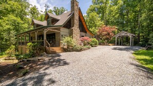 A house with a stone chimney, a covered porch, and a gravel driveway leading to a wooden deck. - Private Log Cabin Near Blowing Rock | Hot Tub, Fire Pit & Creekside Trails (Blowing Rock)