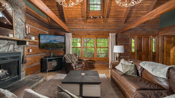 A log cabin interior with a fireplace, leather sofa, stone fireplace, and a television. - Private Log Cabin Near Blowing Rock | Hot Tub, Fire Pit & Creekside Trails (Blowing Rock)