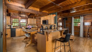 A rustic cabin interior with wooden walls, a kitchen island, bar stools, and a dining table. - Private Log Cabin Near Blowing Rock | Hot Tub, Fire Pit & Creekside Trails (Blowing Rock)