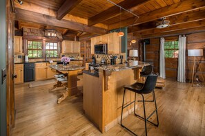 A rustic cabin interior with wooden walls, a kitchen island, bar stools, and a dining table. - Private Log Cabin Near Blowing Rock | Hot Tub, Fire Pit & Creekside Trails (Blowing Rock)