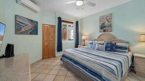 A bedroom with a bed, a nightstand, a ceiling fan, and artwork on the walls. - Peninsula Luxury Condo Vidanta Golf & Beach Access (Los Cabos)
