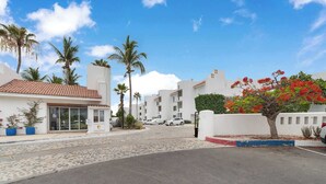 A hotel entrance with a paved driveway, palm trees, and parked cars. - Peninsula Luxury Condo Vidanta Golf & Beach Access (Los Cabos)