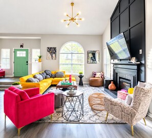 A living room with a yellow sofa, a red armchair, a black entertainment unit, and a fireplace.