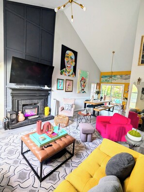 Una sala moderna con chimenea, televisor grande y obras de arte coloridas.