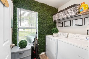 A laundry room with a green wall, two washing machines, a drying rack, and a window with blinds.