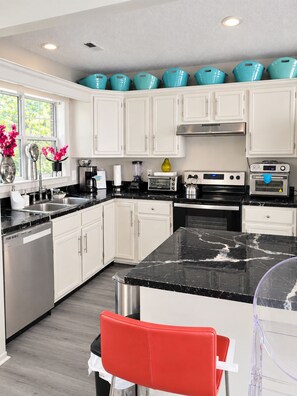 Una cocina moderna con armarios blancos, encimera de mármol negro y una silla roja.