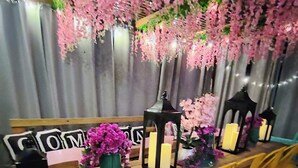 Una mesa dispuesta con velas, jarrones y un cartel.
