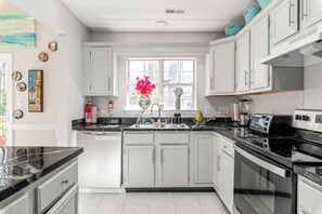 A modern kitchen with white cabinets, black countertops, and stainless steel appliances. - Unique Glamping Artsy Home Charlotte Outdoor Theater Firepit Game Room Downtown (Charlotte)