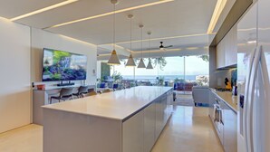 Una cocina moderna con una isla grande, iluminación colgante y una pantalla de televisión amplia.